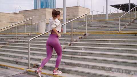 outdoors training in city, woman is running over stairs, tensing legs muscles, townswoman lives healthy lifestyle, keeping fit