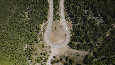 Aerial view of a single car going up on twisty high mountain road among green pine trees