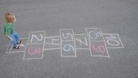 Top view video of little boy's legs and hopscotch drawn on asphalt. Child playing hopscotch game on playground on spring day. Outdoors activities for children.