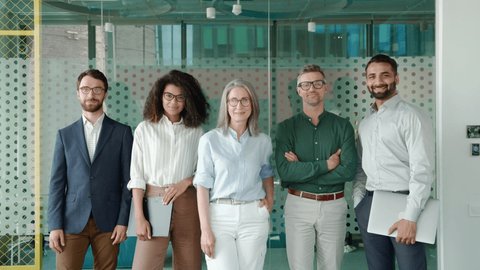 Happy diverse business people team standing together in office, group portrait. Smiling multiethnic international young professional employees company staff with older executive leader look at camera.