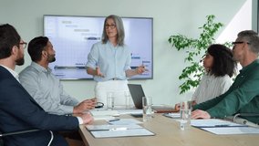 Older senior female mentor leader manager talking to executive team diverse group at boardroom meeting. Multicultural professional business people discuss project plan and financial results in office - Powered by Shutterstock - Get 15% off with code: PIKWIZARD15