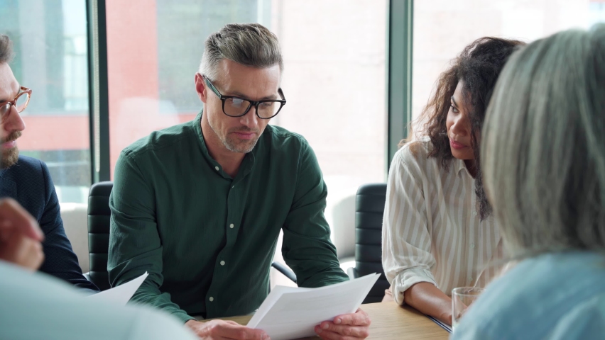 Business man discussing financial contract at executive team meeting. Diverse international business people group negotiating on partnership agreement plan at boardroom table doing paperwork in office Royalty-Free Stock Footage #1076059679