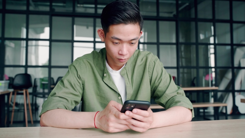 Young happy asian vietnamese student using smartphone gadget social media mobile application on cell phone at desk in modern campus office smiling chatting and texting. Online work education tech. Royalty-Free Stock Footage #1076060030