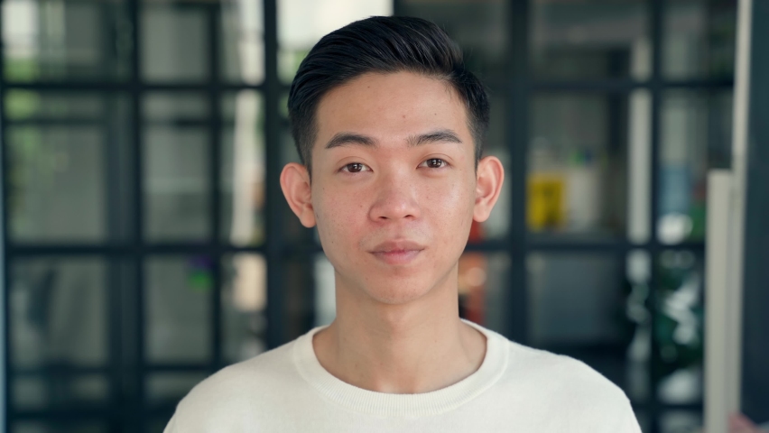 Portrait of young cheerful happy smiling asian chinese high school college university student, IT startup worker standing in contemporary office background looking at camera. Headshot. Close up. Royalty-Free Stock Footage #1076060033