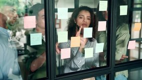 Young happy multiethnic diverse young professional creative team group students talking brainstorming discussing startup project at modern office desk looking at sticky notes on glass. Slow motion. - Powered by Shutterstock - Get 15% off with code: PIKWIZARD15
