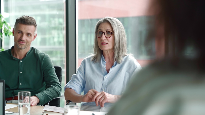Older female mentor leader manager talking to colleagues executive team diverse partners group at executive boardroom meeting. Multicultural professional business people discuss project plan in office | Shutterstock HD Video #1076061563