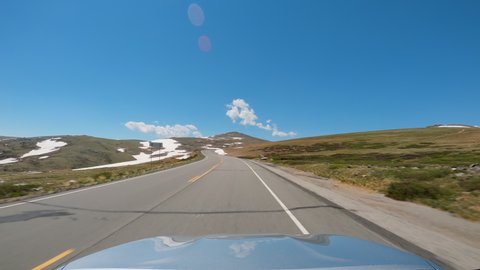 POV Driving a car going up on curvy asphalt road in Montana mountains. Areas of snow and grass on the hill slopes