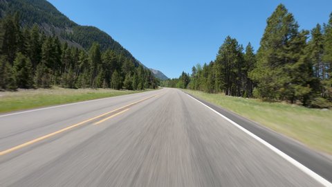 POV Driving a car going up on asphalt road in Montana mountains. Blue sky on sunny day