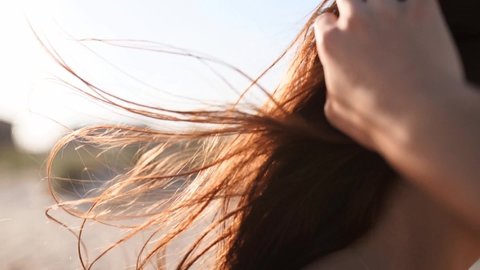 Close back view of brown woman hair tender movement in the air in slow motion 120 fps. Brunette woman in sunglasses walking on sandy beach. Wind blows airy hair shining in sun on sunset. Macro video.