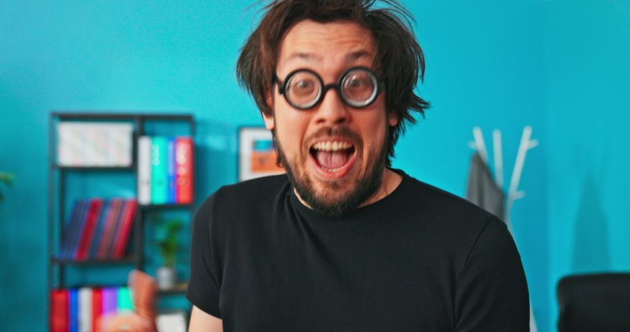 Funny, crazy, strange boy sitting on table with tablet in hand, clicks on screen, shocked look, quickly looks at camera opens face and gestures surprise and astonishment, rolls eyes, blinks few times