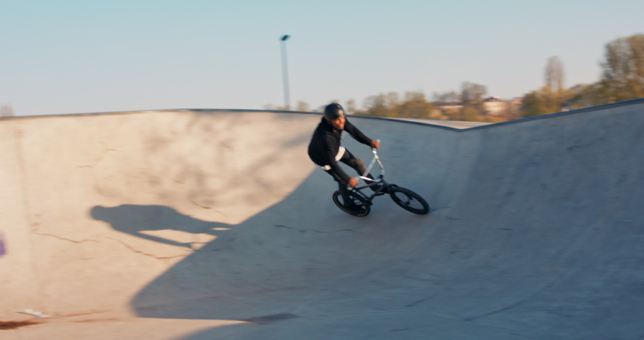 Handsome dark-skinned foreign student rides ramps on low bike, performs tricks, rides high, jumps in the air, is talented, brave, capable Royalty-Free Stock Footage #1076067191