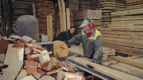 Worker Throws Away Extra Piece Of Wood To Continue Working On Wooden Boards At Saw Mill. Two Men Work At Saw Mill With Team Effort. Manufacturing Wood Materials At Saw Mill. Manual Labor