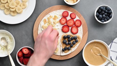 Tortilla cooking process with different fillings of peanut butter, banana, strawberry, blueberry, almond. Food trend. Sweet sandwich for breakfast. Trendy way of wrapping. Top view