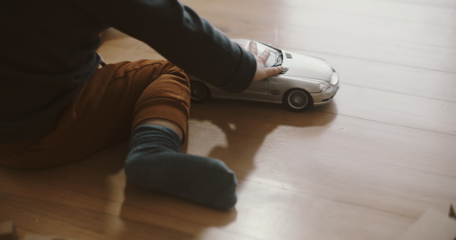 View of childs hands playing silver car model on the wooden floor. Room filled with morning sunlight. Tiny fingers with toys. Royalty-Free Stock Footage #1076068589