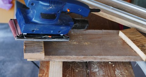 Close-up of orbital sander fixed with clamps on a wooden surface with which a hobbyist smoothes the edges of an OSB board