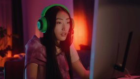 Young asian woman with headphones gamer playing in online video game. Cyber, microphone, live stream, entertainment, gaming, neon, player, enjoy, videogame. Slow motion