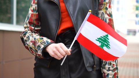 Unrecognizable woman holding Lebanese flag. Girl walking down street with national flag of Lebanon