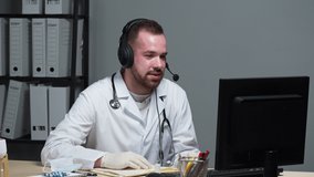 Man doctor with beard wearing medical uniform consulting patient using video call on computer, showing pills, speaking about treatment, male therapist in headphones working remotely at hospital.