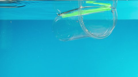 Floating plastic glass with a cocktail tube in the ocean, throwing garbage into the river or lake, water pollution. Rubbish waste in the sea damage the planet, ecological and environmental problems. 