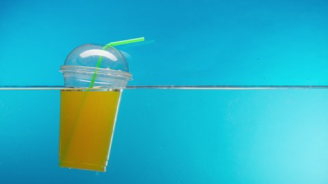 Floating plastic cocktail glass and tube with juice in the ocean, throwing garbage into the river or lake, water pollution. Rubbish waste in the sea damage the planet, environmental problems. 