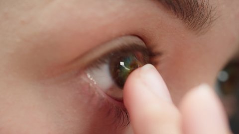 Close-up of a brown-eyed young woman putting on the blue lens with fingers. Optical shop concept. Advertising of contact colorful lenses for make-up and performances, changing color of eyes.