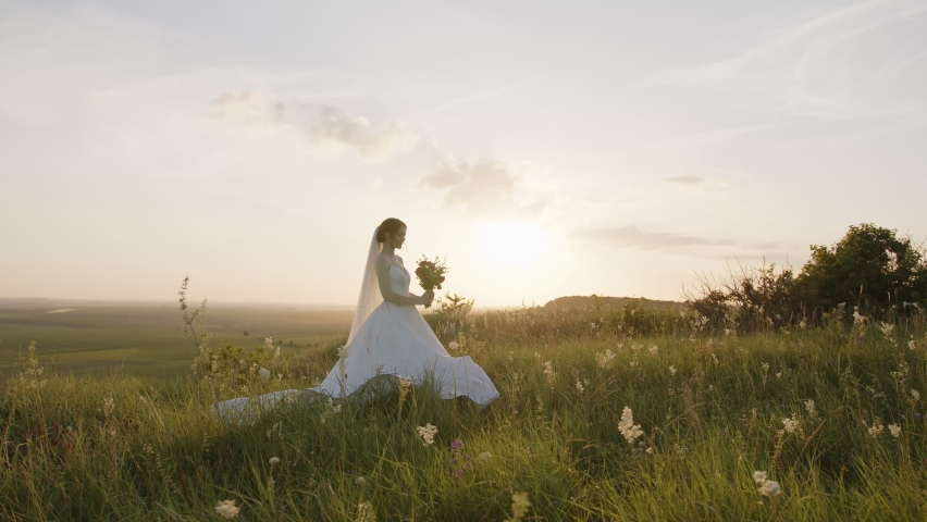 Cute bride holds her bridal bouquet of flowers and smells them, green plants, blue sky