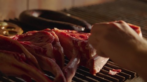 Person rests a tomahawk cut of meat on the grill and gently adjusts it
The cuts are wide and reddish