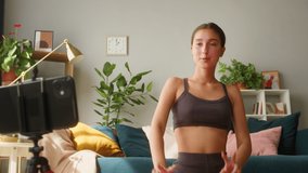 Young female blogger showing exercises for head and neck using video call on smartphone. Keeping fit during self-isolation, coronavirus lockdown, sport remote education online. Concept of home gym.