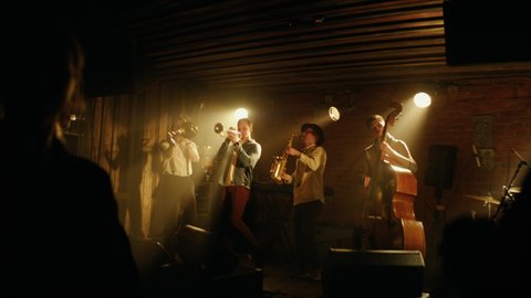 HANDHELD People dancing during concert of a modern jazz band playing on a stage of a small crowded venue. Shot with 2x anamorphic lens