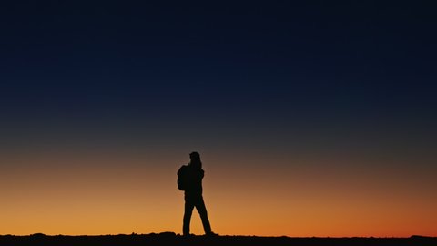 Copy space on deep blue sky background. Incredible view on twilight night sky and dark silhouette of person walking by the edge of mountain in national park enjoying the scenic sunset at high altitude