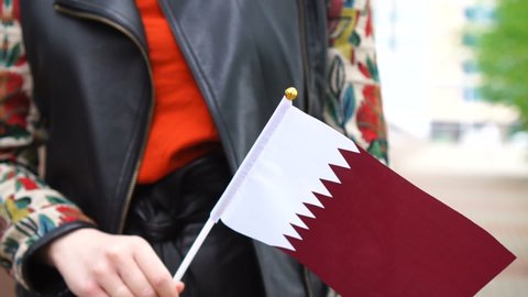 Unrecognizable woman holding Qatari flag. Girl walking down street with national flag of Qatar