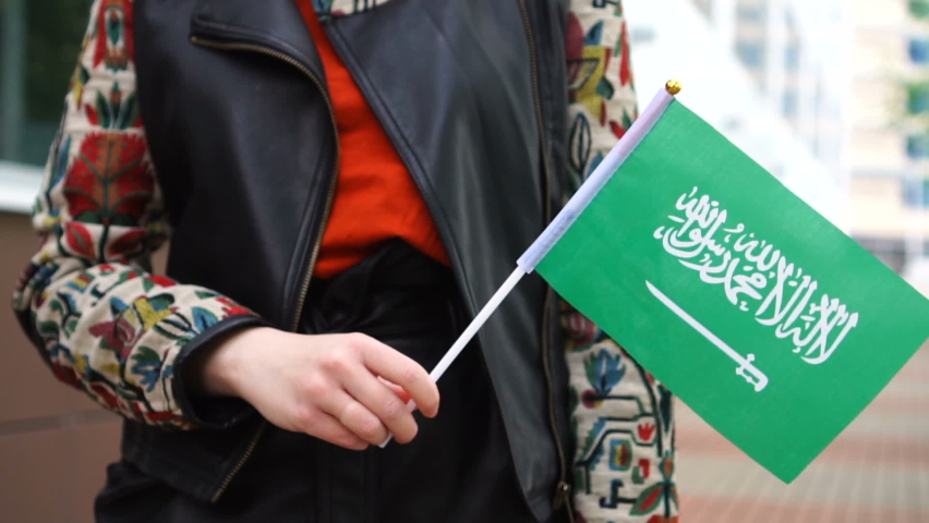 Unrecognizable woman holding Saudi flag. Girl walking down street with national flag of Saudi Arabia Royalty-Free Stock Footage #1076104988