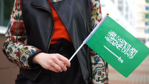 Unrecognizable woman holding Saudi flag. Girl walking down street with national flag of Saudi Arabia