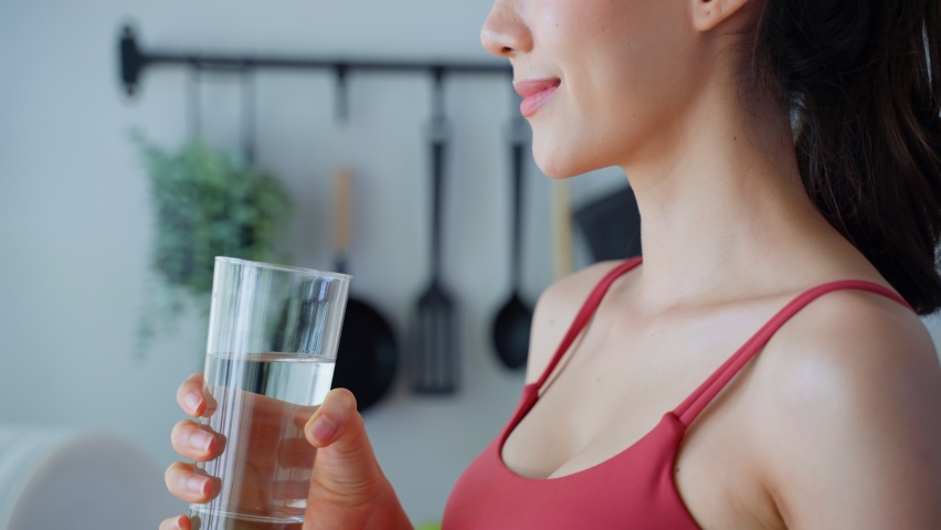 Close up of Asian attractive woman drink water after exercise in house. Young thirsty beautiful sport girl takes a sips of clean mineral natural in cup after workout for health care in kitchen at home Royalty-Free Stock Footage #1076107340