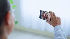Close up of Asian senior elderly woman remote video call with family. Happy Older grandparent hold mobile phone to talk virtual online with young couple and grandchild children in living room at home.
