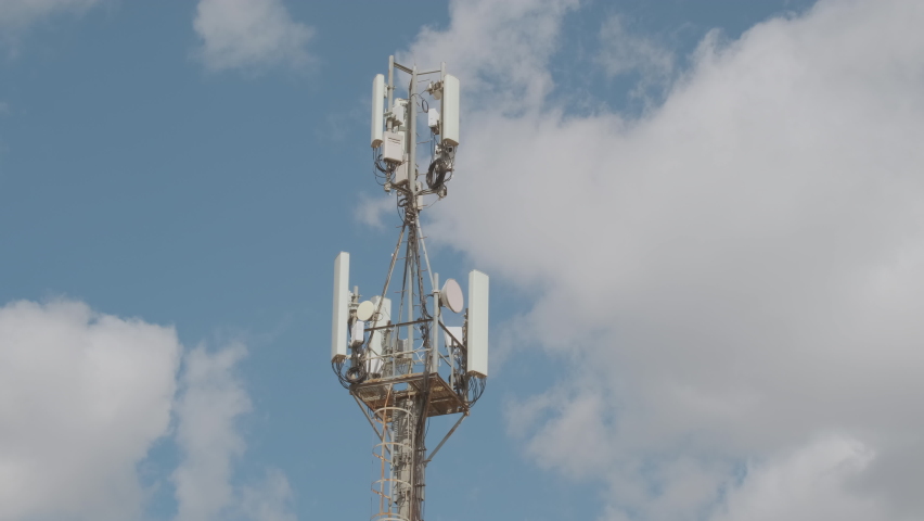 Cell tower on background of blue sky with running clouds in city, time lapse. Cellular base station with mobile antenna transmits signal to 5G, extension of coverage. Royalty-Free Stock Footage #1076113670