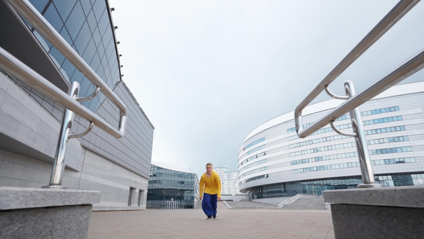 Free running, young man runs over obstacles in the city and doing a flips on training area near modern buildings.