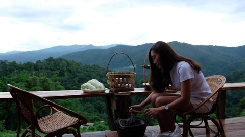 An asian woman preparing and lighting fire in a stove before cooking Moo Kata, Thai barbecue grill pork on balcony with beautiful nature view