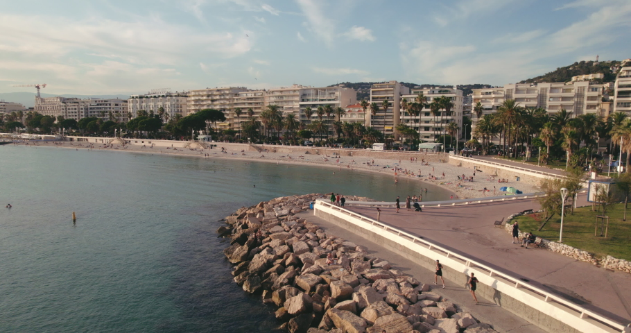 Aerial vidéo of seaside with tourists and joggers, city, beach, mountain and blue sky with clouds on the horizon. La Croisette in Cannes, France. Royalty-Free Stock Footage #1076118950