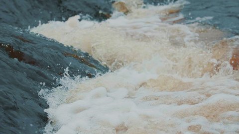 Strong flow of water with splashes and foam in slow motion. Powerful raging river flow. Extreme steep river threshold. Emergency water discharge. Dam break, spring flood, dangerous weather conditions.
