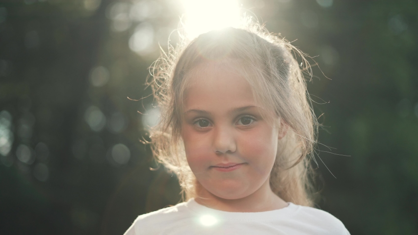 Happy girl in rays of the sun. Girl face in park close-up. Dream girl. Happy face of a child in rays of sun. Child smiles at camera. Girl dream. Face close-up. Happy child in park.Beautiful face Royalty-Free Stock Footage #1076126774