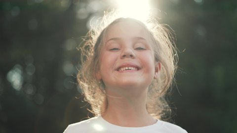 Happy girl in rays of the sun. Girl face in park close-up. Dream girl. Happy face of a child in rays of sun. Child smiles at camera. Girl dream. Face close-up. Happy child in park.Beautiful face