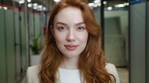 Beautiful smiling redhead young woman pretty face looking at camera posing alone at office, happy millennial female student professional close up. Wearing formal wear