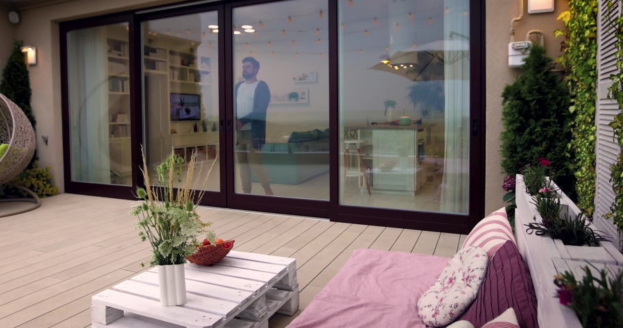 man opens wooden sliding doors, going out on rooftop patio with cozy lounge zone Royalty-Free Stock Footage #1076131328