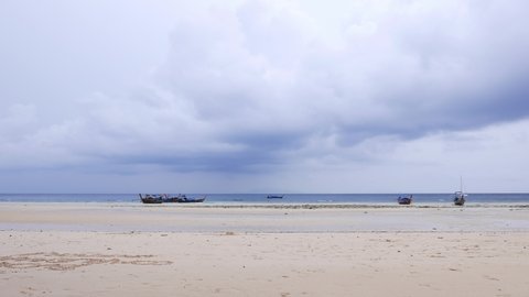 Empty tropical beach, low tide and rainy weather, long tail boats in low water or stranded. Loh Moo Dee beach at Phi Phi Don island. Rain bearing clouds hand over sea