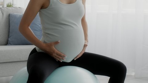 Pregnant Woman Doing Exercises On Fitness Ball At Home, Closeup Shot Of Expecting Woman With Big Belly Training On Fitball In Living Room Interior, Getting Ready For Childbirth, Slow Motion Footage