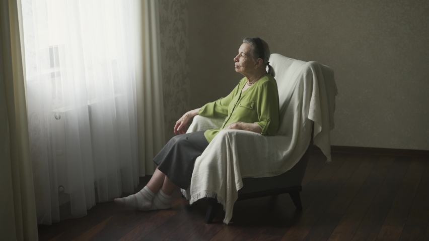 Senior woman sitting on armchair and looks outside the window Royalty-Free Stock Footage #1076138816