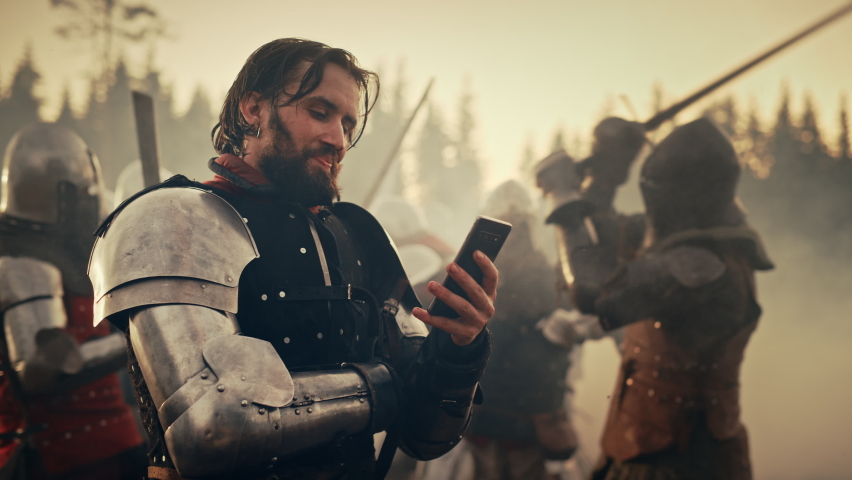 Portrait of Handsome Medieval Knight Using Smartphone on Battlefield, Smiling. Fun Concept: Successful Armored Warrior Ordering Online, Betting, Investing, doing E-commerce. War is Raging Royalty-Free Stock Footage #1076140769