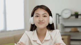 Young asian woman wearing headphone look at camera video conference online sitting in living room at home. Business Woman look at screen Meeting on social media live steam. Work, learning from home.