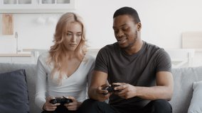 African American Boyfriend Explaining Discontented Girlfriend How To Play Video Game Sitting On Sofa At Home. Multiethnic Couple Playing Videogames Spending Weekend Together Indoor